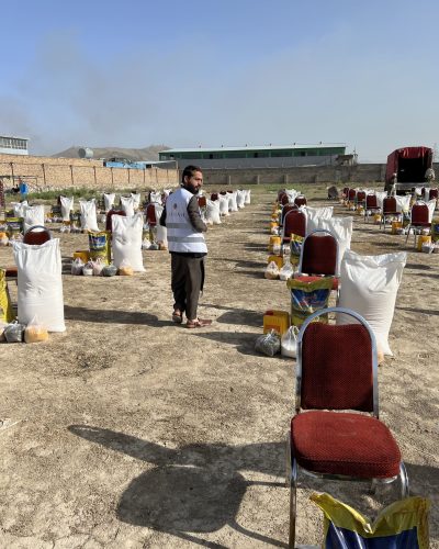 Hier sind viele Reihen von roten Stühlen. Davor stehen viele Säcke mit Reis und anderen Lebensmitteln. Diese werden bei der Lebensmittelverteilung im Ramadan verteilt.